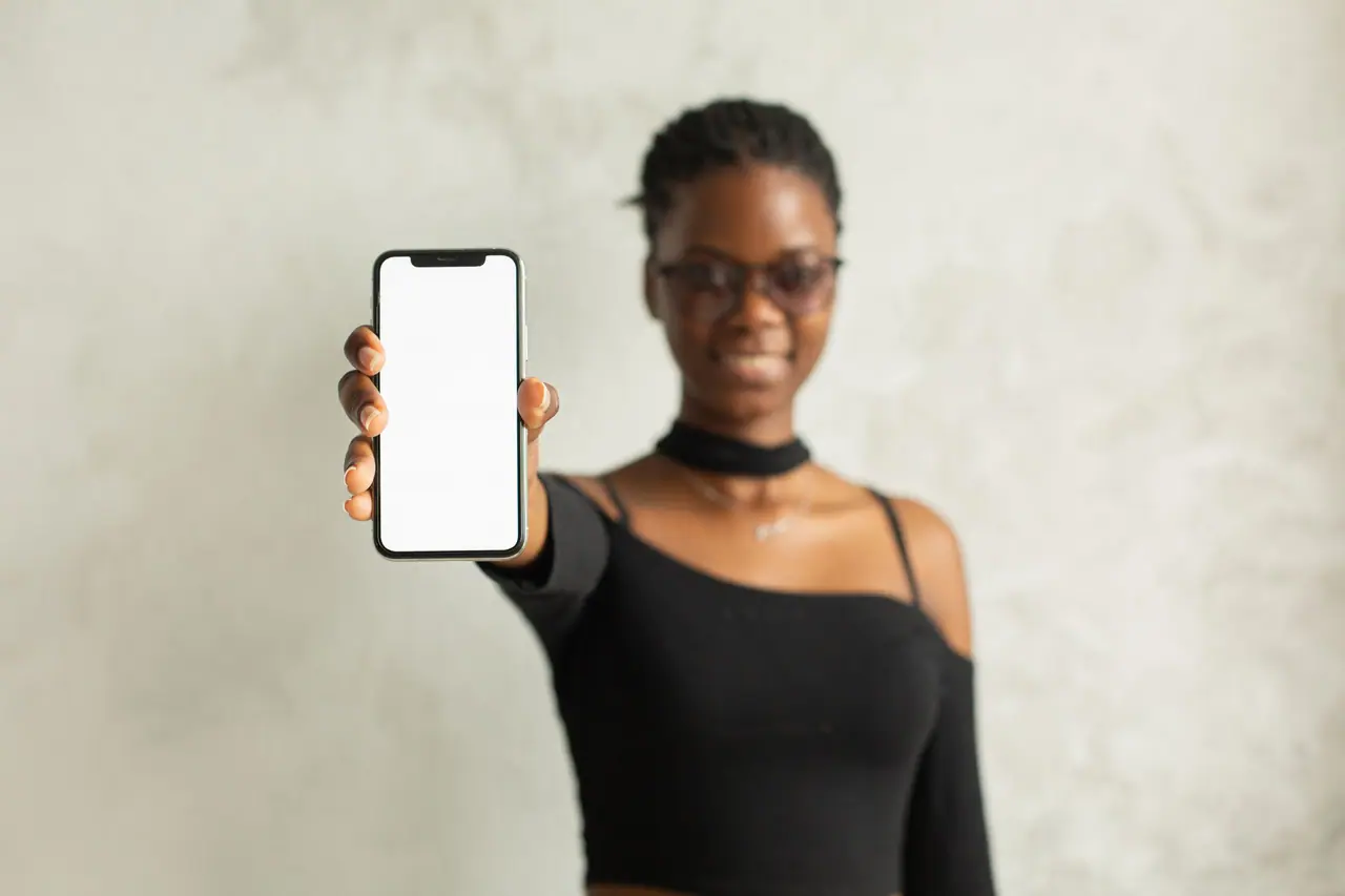 Mujer que sonríe y muestra la pantalla de su celular